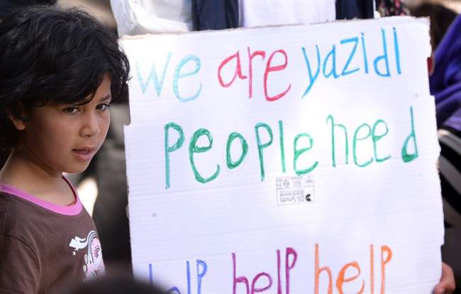 A child stands next to a placard reading "We are Yazidi people, Need Help Help Help", prior to the arrival of Pope Francis at the Moria refugee camp, on the Greek island of Lesbos, Saturday, April 16, 2016.