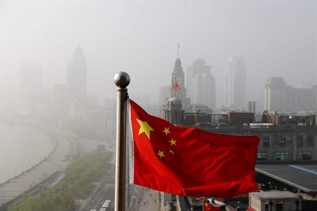 FILE - A Chinese national flag flutters against the office buildings at the Shanghai Bund shrouded by pollution and fog in Shanghai, China, Thursday, April 14, 2016.