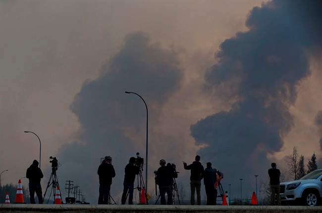 Media watch as smoke billows in the sky near a wildfire in Fort McMurray, Alta., on Friday, May 6, 2016. The Alberta provincial government, which declared a state of emergency, said more than 1,100 firefighters, 145 helicopters, 138 pieces of heavy equipment and 22 air tankers were fighting the fire, but Chad Morrison, Alberta's manager of wildfire prevention, said rain is needed. 