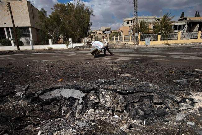 In this Thursday, April 14, 2016 photo, a Syrian man pushes a trolley with his belongings to load them onto a bus with others leaving their home towns, near a crater in the town of Palmyra in the central Homs province, Syria. 