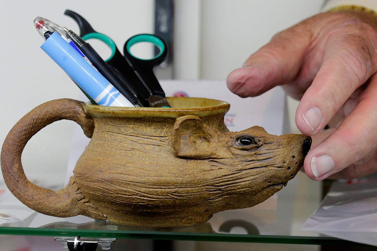 Auctioneer Bob Sheehan reaches for a pottery mug, in the shape of a rat, which contains pens, that are among items belonging to James "Whitey" Bulger and Catherine Greig.