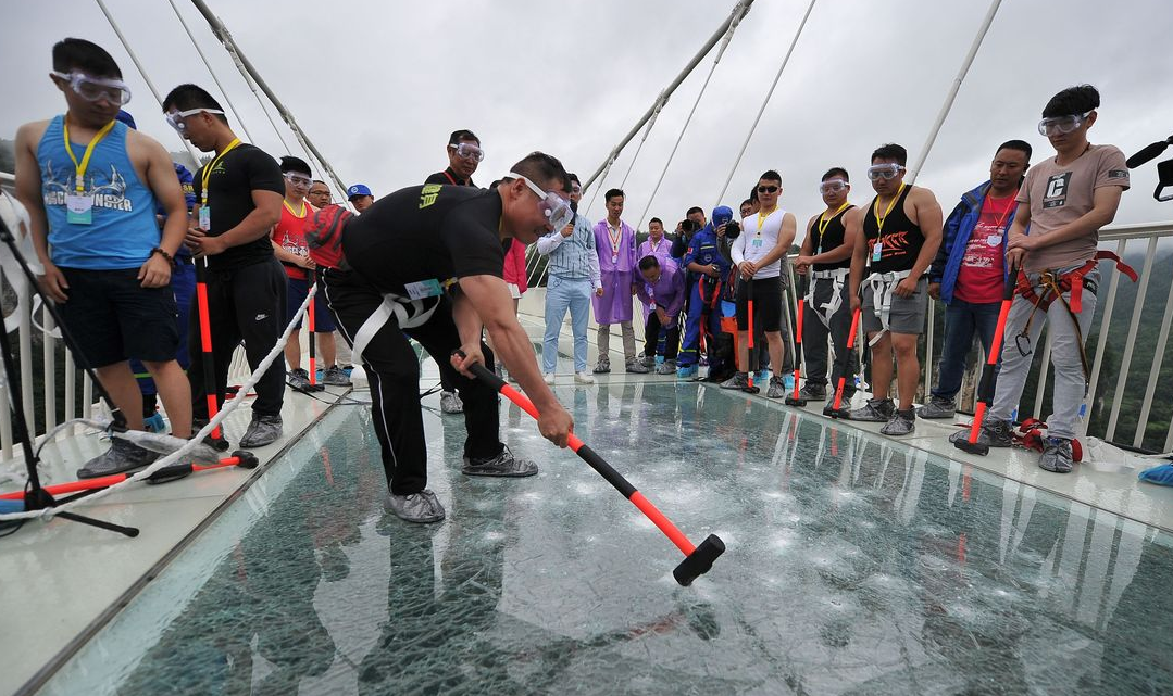 A man swings a hammer against the glass bridge. 