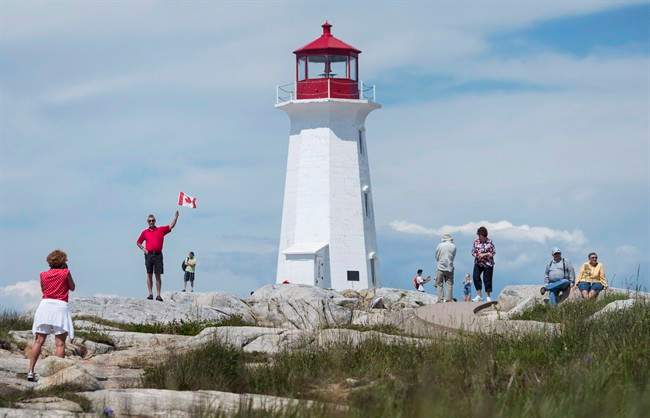 Keith Boutilier, second from left, poses with a Canadian flag for his wife France Boutilier, left, in Peggy's Cove, N.S., on Canada Day, July 1, 2016.