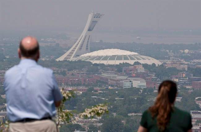 Tourists look through out through smog at Montreal's Olympic Stadium in a May 31, 2010, file photo. It's been dubbed the "Big Owe" for its runaway construction costs and it has attracted widespread derision for falling concrete and roof rips but Montreal's Olympic Stadium doesn't just have detractors.