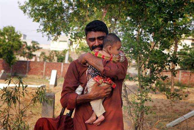 In this June 18, 2016 photo, Mohammed Tofeeq cries as he holds his 10-month-old daughter, Gulshan Tofeeq, at the grave of his wife Muqadas Tofeeq, who local police say was killed by her mother, in Butrawala village on the outskirts of Gujranwala, Pakistan.