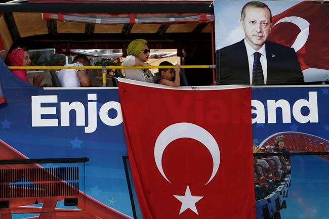 People sit on a tour bus with Turkish flags and a portrait of the Turkish President Recep Tayyip Erdogan in Taksim square in Istanbul, Monday, July 25, 2016.