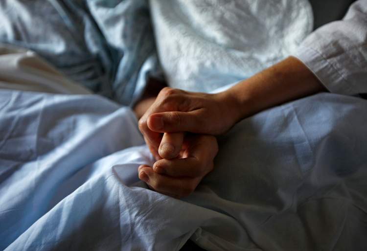 A woman holds the hand of her mother who is dying from cancer during her final hours at a palliative care hospital in Winnipeg in this image from 2010. 