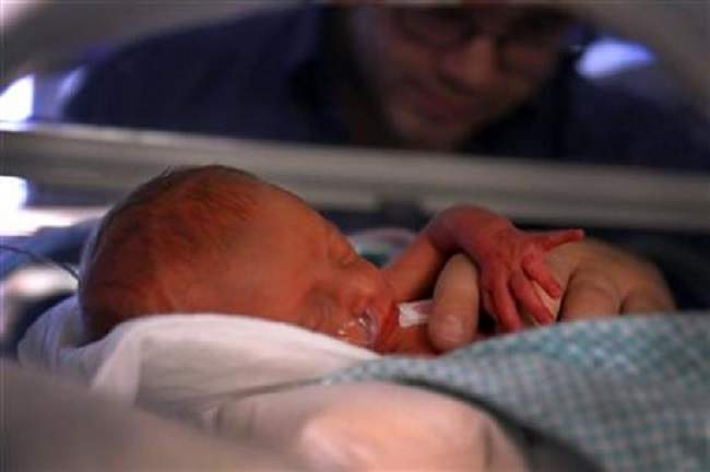 First-born of the triplets, Raelyn stretches in her isolette while her father Logan Fletcher holds her.