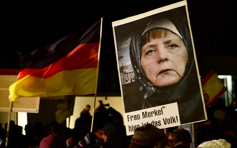 A protestor holds a poster with an image of German Chancellor Angela Merkel wearing a headscarf in front of the Reichstag building with a crescent on top during a rally of the group Patriotic Europeans against the Islamization of the West, or PEGIDA, in Dresden, Germany.  Words on poster read : "Mrs. Merkel, here is the people." .