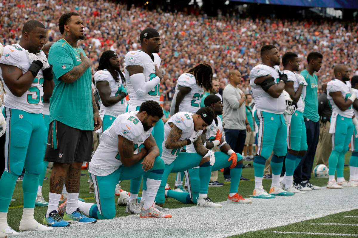 Miami Dolphins Arian Foster (29), Kenny Stills (10) and Michael Thomas (31) kneel during the national anthem before an NFL football game against the New England Patriots Sunday, Sept. 18, 2016, in Foxborough, Mass. 