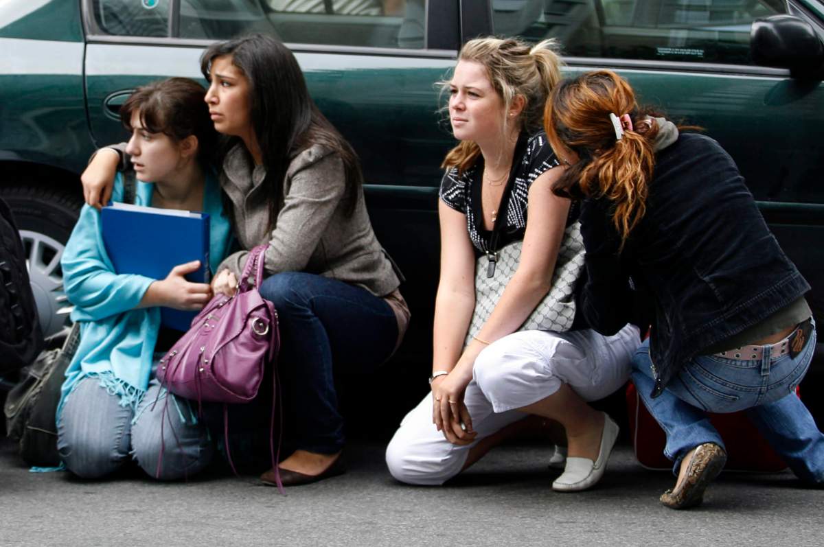 Students take cover behind a car at Dawson College after reports of a gunman in the building in Montreal, Wednesday, Sept.13, 2006.