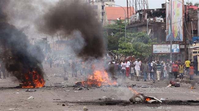People stand near burning debris during election protests in Kinshasa, Democratic Republic of Congo, Monday, Sept. 19, 2016. Witnesses say at least four people are dead after opposition protests against a delayed presidential election turned violent in Congo's capital. The protests were organized by activists who are opposed to longtime President Joseph Kabila, who is now expected to stay in office after his mandate ends in December. 