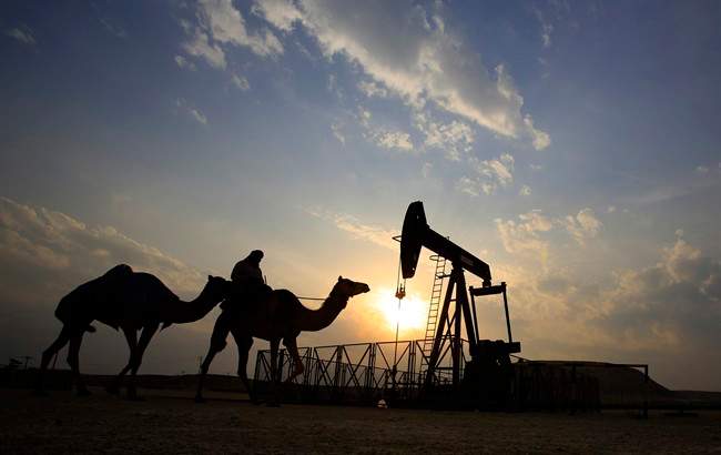FILE- In this Sunday, Dec. 20, 2015 file photo, a man rides a camel through the desert oil field and winter camping area of Sakhir, Bahrain. OPEC nations have agreed in theory that they need to reduce their production to help boost global oil prices during a meeting in Algeria, but a major disagreement between regional rivals Saudi Arabia and Iran still may derail any cut. (AP Photo/Hasan Jamali, File).