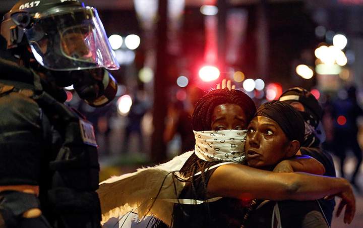 Two women embrace while looking at a police officer in uptown Charlotte, NC during a protest of the police shooting of Keith Scott, September 21, 2016.