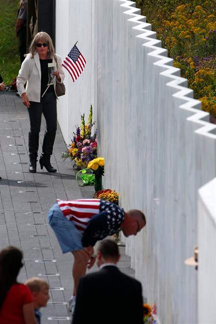 In this Sept. 11, 2015 file photo, Suzi Balco, of St. Joseph, Mich., top left, places a flag at the name of Todd Beamer at the Wall of Names after a Service of Remembrance at the Flight 93 National Memorial in Shanksville, Pa. Victims’ relatives and dignitaries will convene Sunday, Sept. 11, 2016, at the site for one of the constants in how America remembers 9/11 after 15 years, the anniversary ceremony itself.