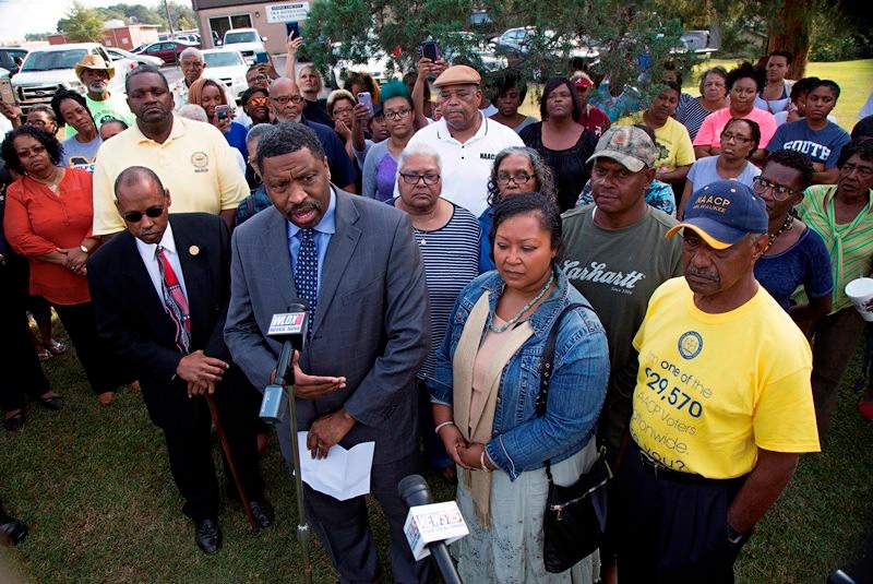 Derrick Johnson, left, president of the Mississippi NAACP, center left, talks to the media on behalf of Stacey Payton, center right, and Hollis Payton, behind his wife Stacey, in front of the Stone County Courthouse in Wiggins, Miss., Monday, Oct. 24, 2016. 