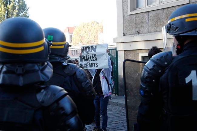 A man holds a poster reading "No to migrants roundup" as police officers control migrants in Paris, Monday, Oct. 31, 2016. 