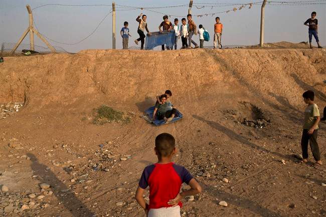 Children use a piece of plastic to slide down a slope at the Baharka camp for displaced persons on the outskirts of Irbil, Iraq, Tuesday, Oct. 25, 2016. Nearby Mosul, the largest city controlled by the Islamic State group, is still home to more than 1 million civilians. (AP Photo/Marko Drobnjakovic).