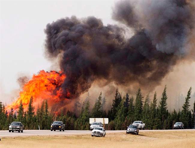 A convoy of evacuees from Fort McMurray, Alberta drive past wildfires that are still burning out of control as they leave the city Saturday, May 7, 2016. 