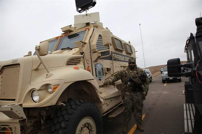 A member of the Stutsman County SWAT team who declined to give his name nor to be identifiable by badge stands guard by an armoured personnel carrier equipped with an LRAD, or long range acoustic device, while deployed to watch protesters demonstrating against the Dakota Access Pipeline encroaching the water source near the Stand Rock Sioux Reservation, in Cannon Ball, N.D., Sunday, Oct. 30, 2016.