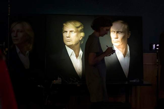 A journalist writes a material as she watches a live telecast of the U.S. presidential election standing at portraits of U.S. presidential candidate Donald Trump and Russian President Vladimir Putin in the Union Jack pub in Moscow, Russia, Wednesday, Nov. 9, 2016.