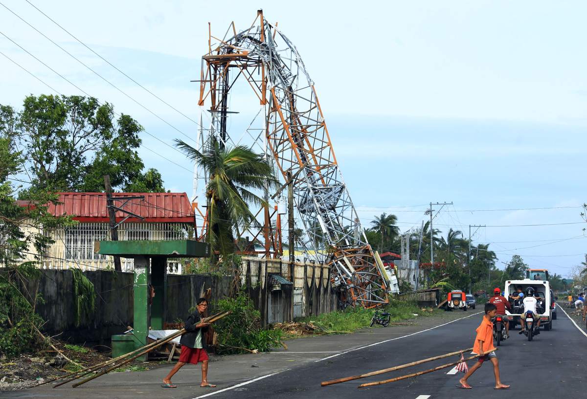 Residents walk past a downed cell network tower in Polangui, Albay province on December 26, 2016.Typhoon Nock-Ten, which made landfall on the eastern island province of Catanduanes on December 25, is forecast to move westward towards the country’s heartland, packing winds of 215 kilometres (134 miles) per hour. / AFP / CHARISM SAYAT (Photo credit should read