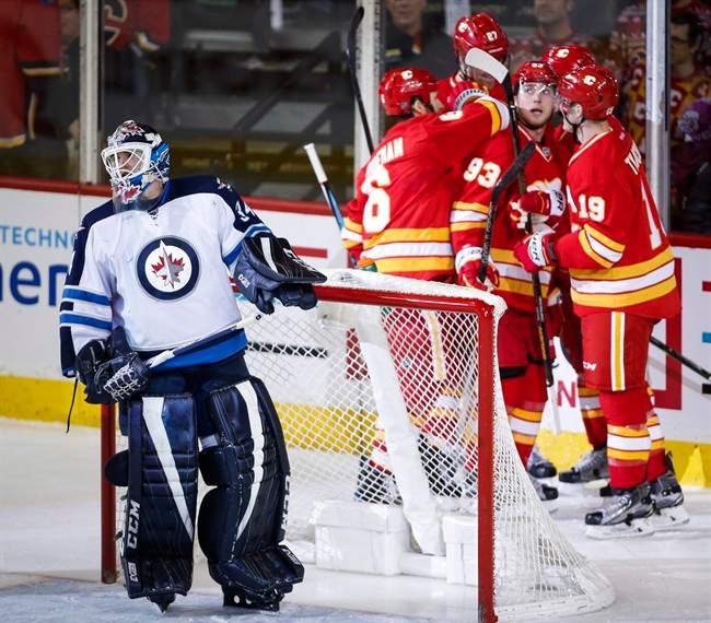 Winnipeg Jets goalie Michael Hutchinson, left, looks away as Calgary Flames celebrate their fourth goal during second period NHL hockey action in Calgary, Saturday, Dec. 10, 2016.