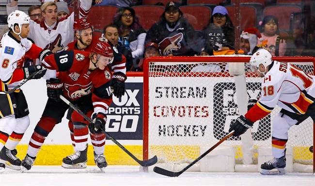 Arizona Coyotes center Christian Dvorak (18) scores a goal past Calgary Flames center Matt Stajan (18) and defenseman Dennis Wideman (6) while Coyotes right wing Josh Jooris (86) looks on during a first period of an NHL hockey game Monday, Dec. 19, 2016, in Glendale, Ariz. 
