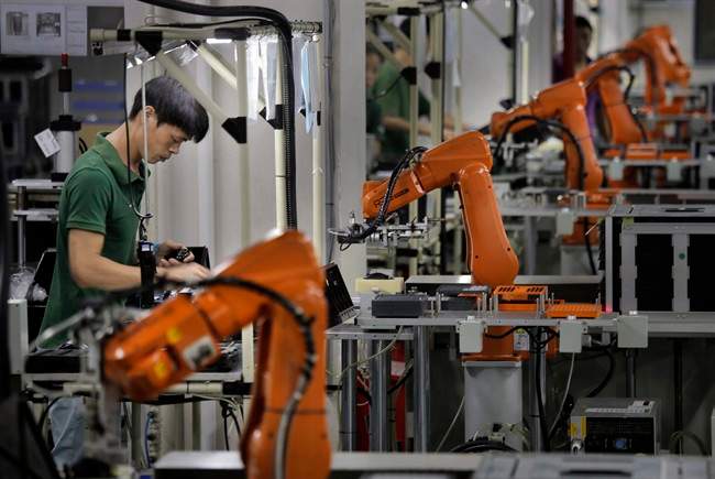 In this Aug. 21, 2015 photo, a man works amid orange robot arms at Rapoo Technology factory in southern Chinese industrial boomtown of Shenzhen. 