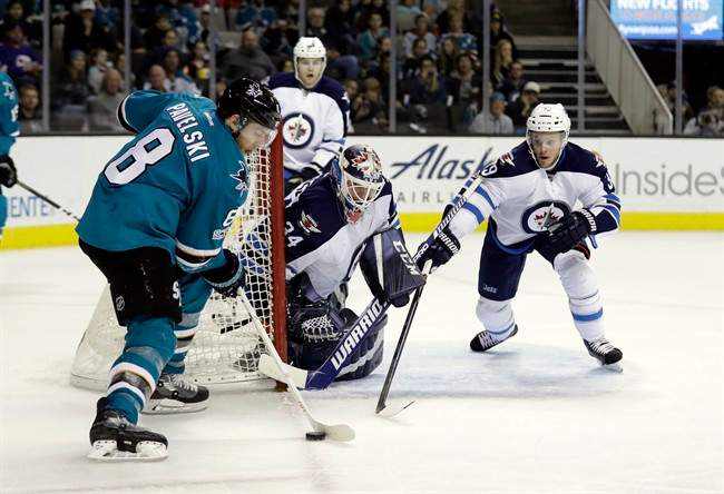 San Jose Sharks' Joe Pavelski (8) controls the puck in front of Winnipeg Jets goalie Michael Hutchinson (34) and Toby Enstrom, right, during the second period of an NHL hockey game, Monday, Jan. 16, 2017, in San Jose, Calif.