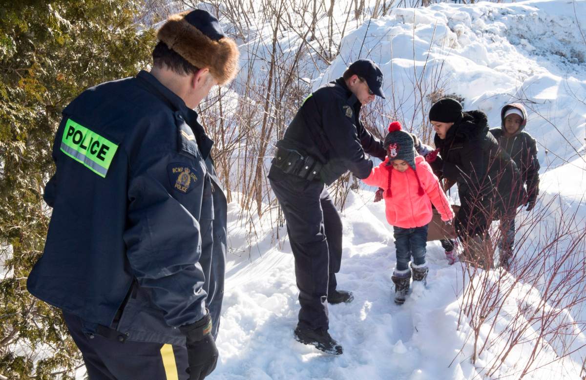 Family members from Somalia are helped into Canada by RCMP officers along the U.S.-Canada border near Hemmingford, Que., on Friday, Feb. 17, 2017. A number of refugee claimants are braving the elements to illicitly enter Canada.