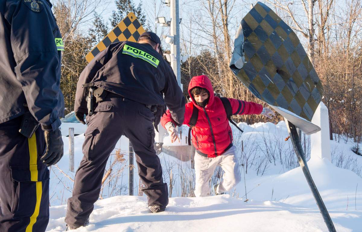 An RCMP officer extends his hand to help a young man from Yemen to cross into Canada at the U.S.-Canada border in Quebec, on Feb. 17. A number of refugee claimants are braving the elements to illicitly enter Canada.