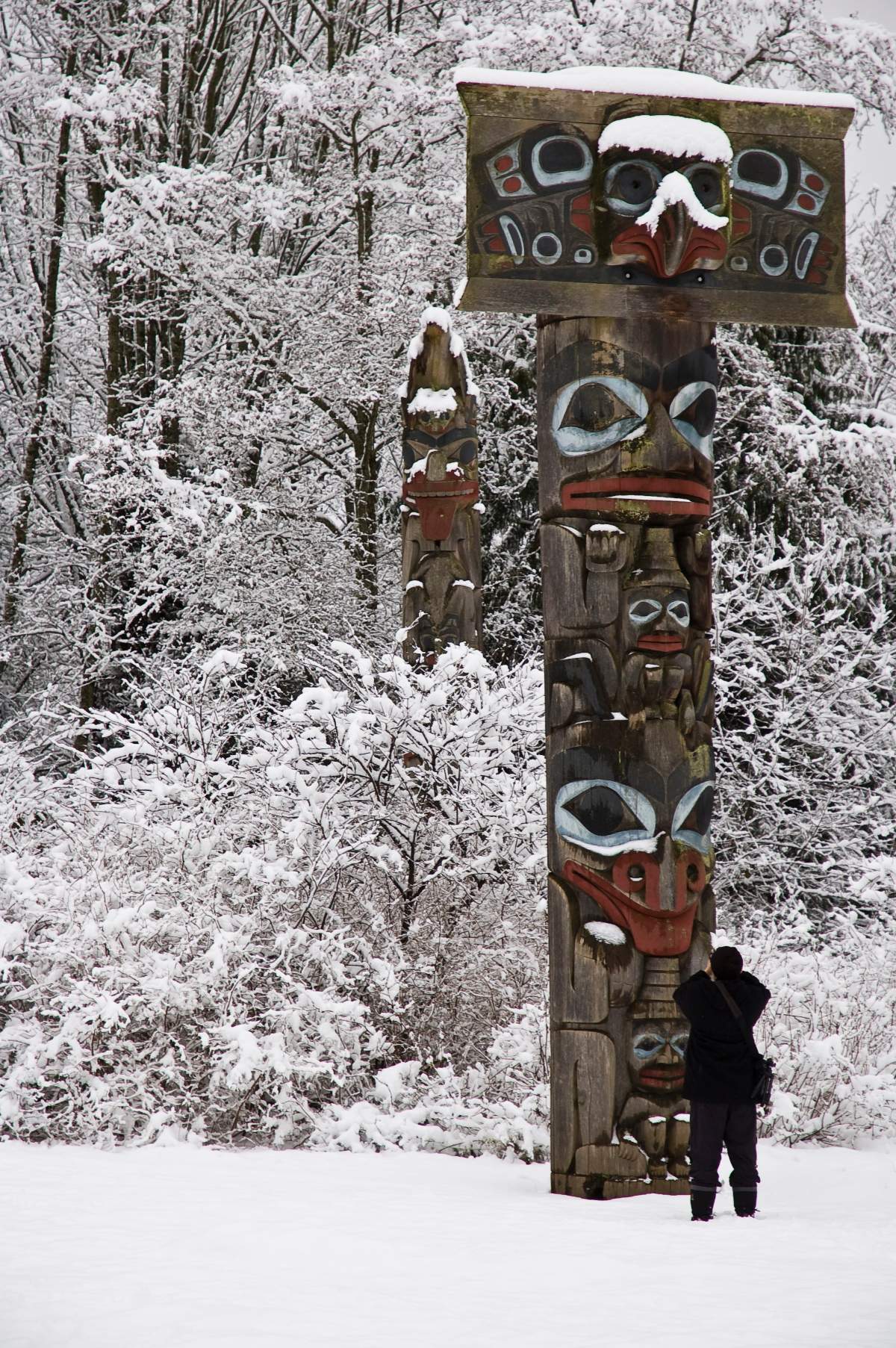 A person stops to take a photograph of a snow-covered totem pole at the Haida House exhibit at the University of Briitish Columbia’s Museum of Anthropology.