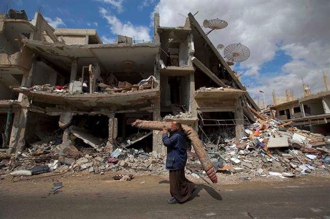 In this April 14, 2016 file photo, a Syrian man carries a carpet through a devastated part of the town of Palmyra as families load their belongings onto buses in the central Homs province in Syria. 