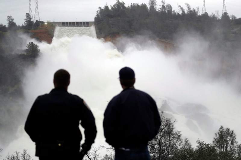 Two men watch as water gushes from the Oroville Dam’s main spillway Wednesday, in Oroville, Calif.