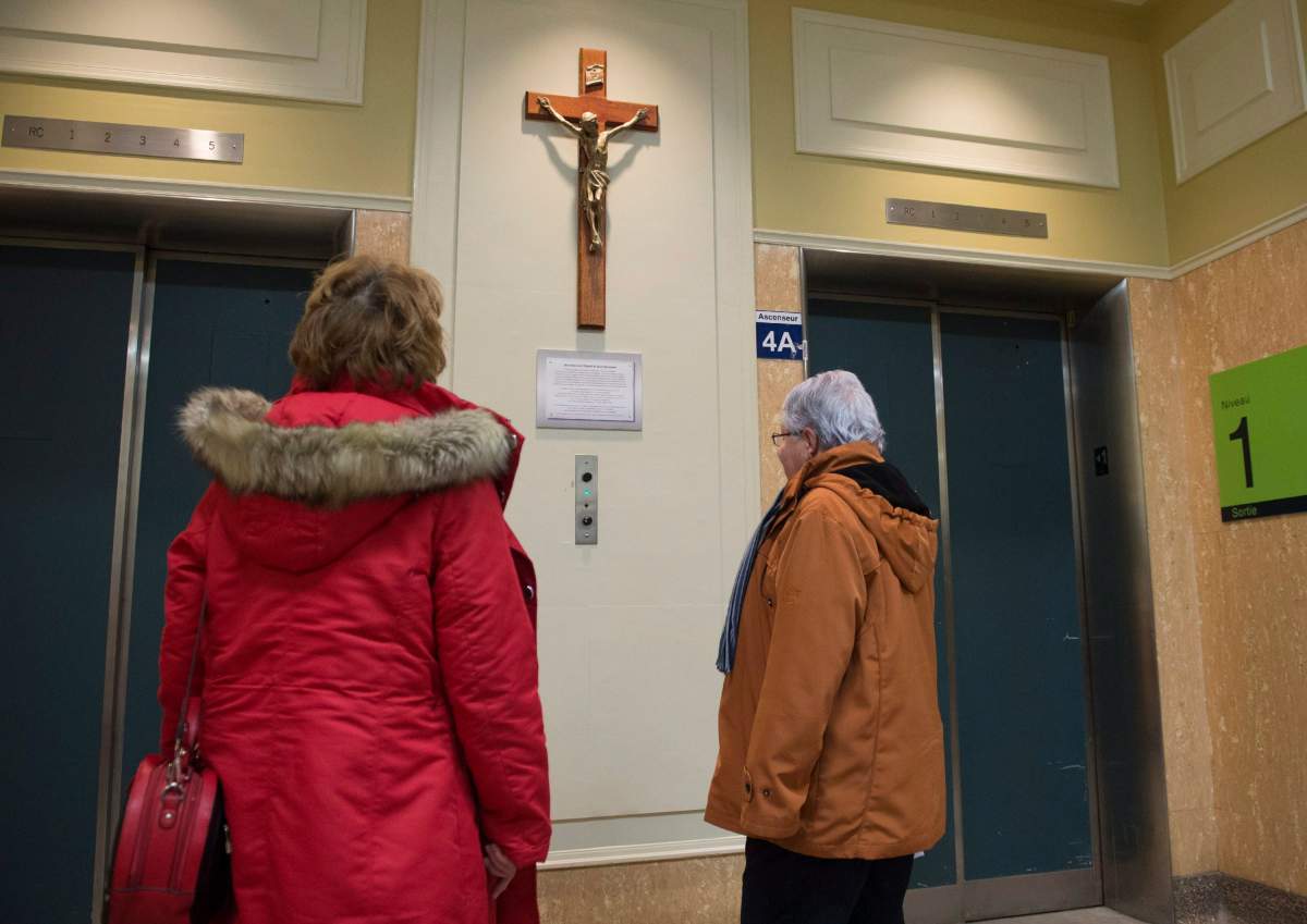 People look at a crucifix before going up the elevator at the main entrance of the Saint-Sacrement hospital, Thursday, March 2, 2017 in Quebec City. The crucifix that was taken off the wall after a complaint and was re-installed by the establishment after numerous critics from citizens.