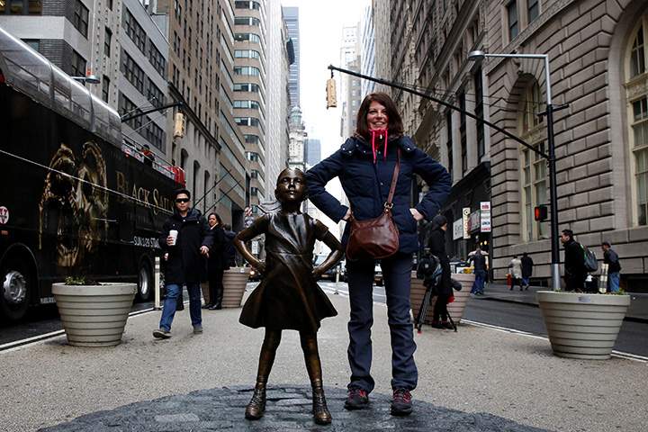 A woman poses next to a statue of a girl facing the Wall St. Bull in the financial district in New York, U.S., March 7, 2017.
