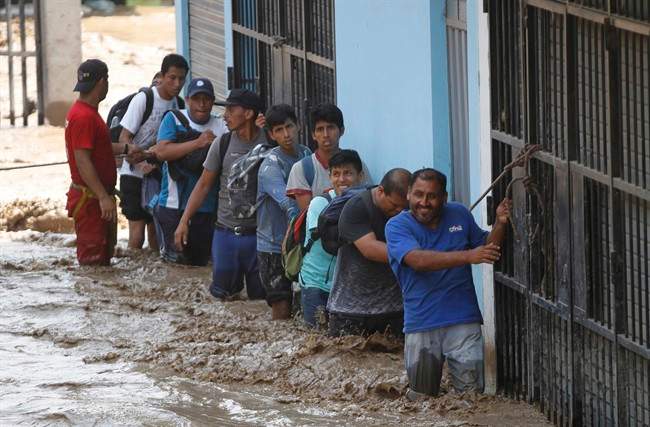 A group of people, stranded in flood waters, hold onto a rope as they walk to safety in Lima, Peru, Friday, March 17, 2017. Intense rains and mudslides over the past three days have wrought havoc around the Andean nation and caught residents in Lima, a desert city of 10 million where it almost never rains, by surprise.