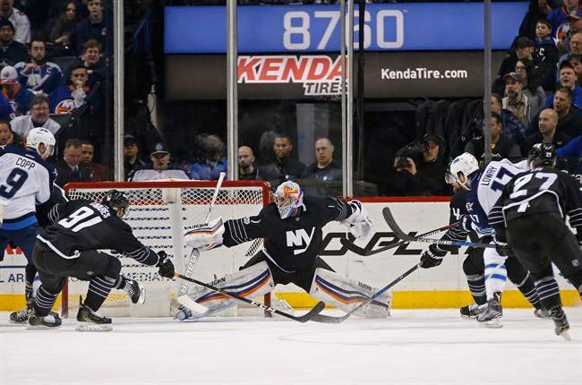 Winnipeg Jets center Adam Lowry scores as the puck sails beyond the reach of New York Islanders goalie Thomas Greiss of Germany with Islanders center John Tavares trying in vain to block it during the second period of an NHL hockey game.