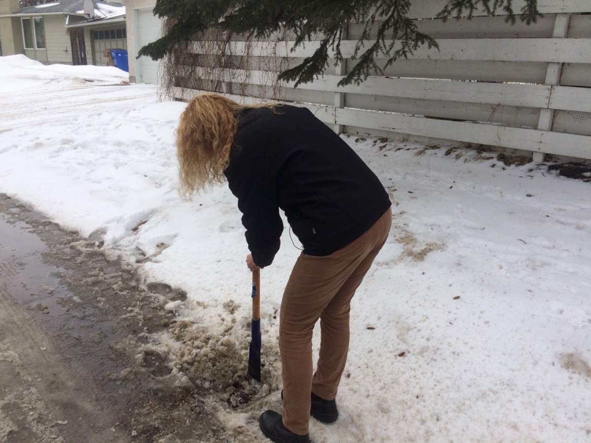 A woman chips away ice and snow frozen on a catch basin near her home.