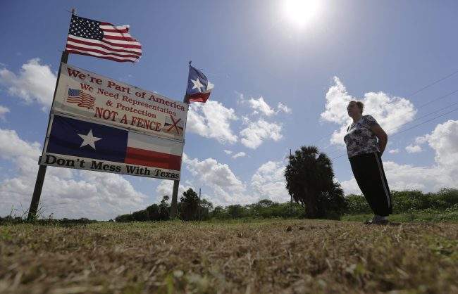 Pamela Taylor, whose home is on the south side of the border fence, stands near a sign she erected, in Brownsville, Texas, Sept. 17, 2015.