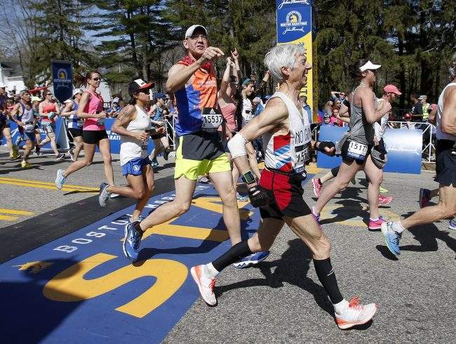 Leeland Cole-Chu (15537) identifies Ben Beach, center, as he crosses the start line running his 50th consecutive Boston Marathon at the start of the race in Hopkinton, Mass., Monday, April 17, 2017.