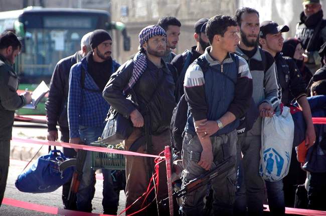 In this photo released by the Syrian official news agency SANA, Syrian opposition fighters hold their weapons as they prepare to board a bus to leave the last rebel-held neighborhood of al-Waer in Homs province, Syria, Monday, April 24, 2017.