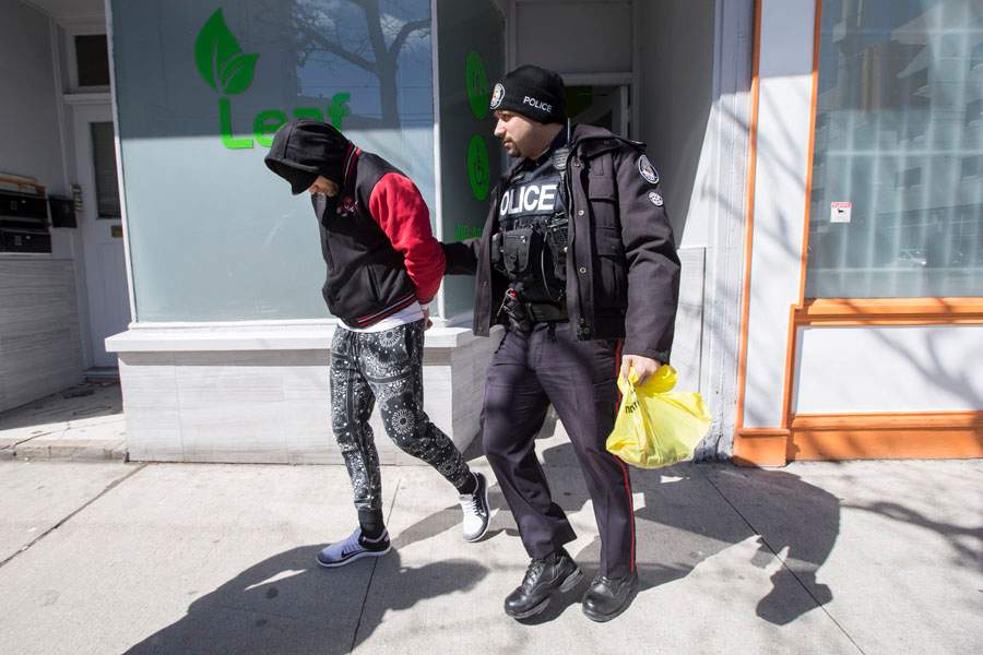 A man is led away in handcuffs during a series of arrests at a Toronnto marijuana dispensary in April 2017.