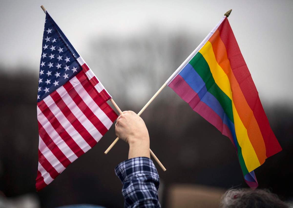 A participant holds both the U.S. national flag (L) and the LGBT community's symbolic  Rainbow flag (R) as people arrive on the mall for the Million Woman March in Washington in January. 