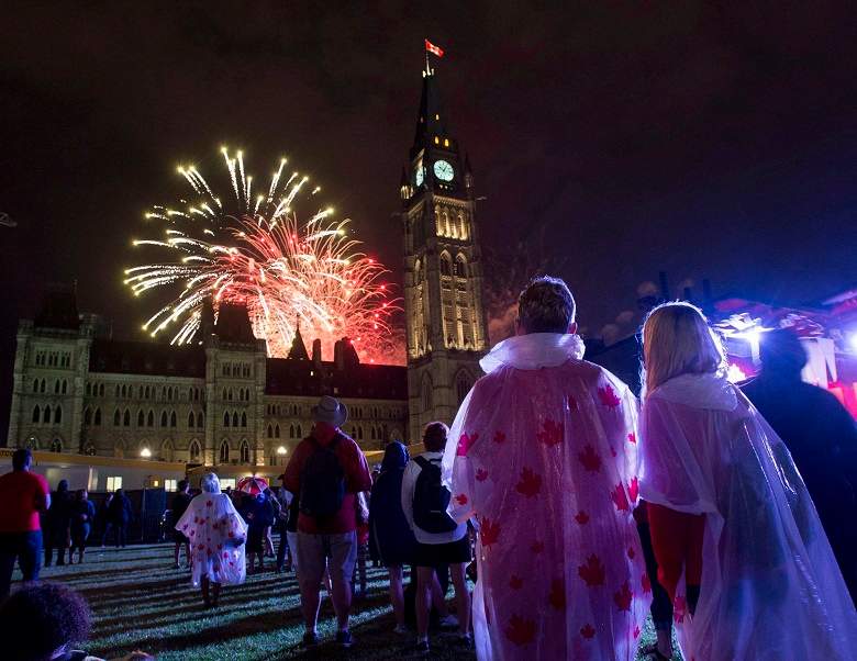 People watch fireworks as they explode behind the Peace Tower during Canada Day celebrations on Parliament Hill on Friday, July 1, 2016 in Ottawa. THE CANADIAN PRESS/Justin Tang