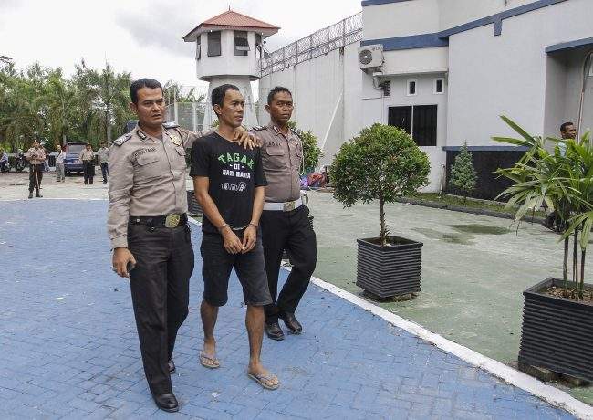 Police officers escort a captured inmate following a prison break at the Sialang Bungkuk Prison in Pekanbaru, Riau province, Indonesia, Saturday, May 6, 2017.