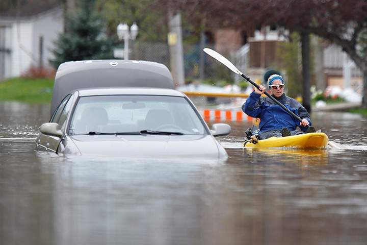 A woman paddles a kayak past an abandoned car on a flooded residential street in Gatineau, Quebec, May 4, 2017.