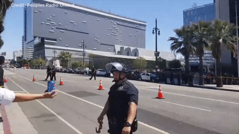 A May Day demonstrator in Los Angeles pokes fun at Pepsi and Kendall Jenner by handing LAPD officer a can of soda.