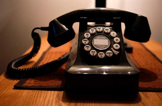 A black landline telephone on a wooden desk.